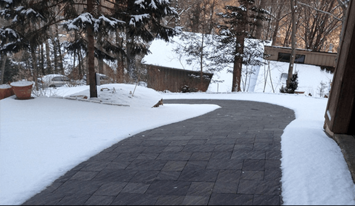 Heated driveway clearing snow while surrounding area remains covered